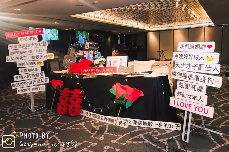 心心相印婚宴拍貼區佈置,兩側立著趣味標語手舉牌與大型囍字、玫瑰花道具